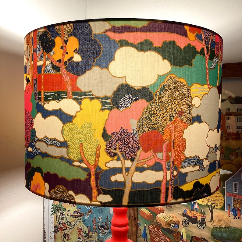 May include: A colourful lampshade with a whimsical design featuring trees, clouds, and a landscape. The lampshade is made of fabric and has a textured surface.