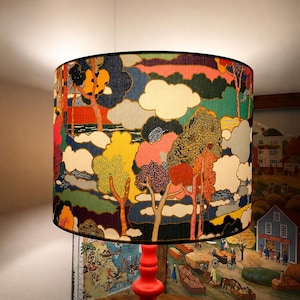 K&ouml;nnte beinhalten: Zylindrischer Lampenschirm mit farbenfrohem Landschaftsdesign. Das Kunstwerk zeigt B&auml;ume, Wolken und eine Vielzahl von Farben, darunter Rot, Gelb, Blau und Gr&uuml;n. Der Lampenschirm ist auf einem roten Lampenfu&szlig; montiert.