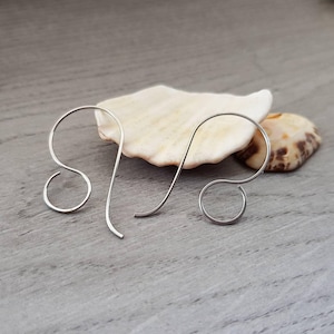 May include: Two silver earring hooks, also known as French hooks, are shown on a light grey surface. The hooks are made of metal and have a simple, elegant design.