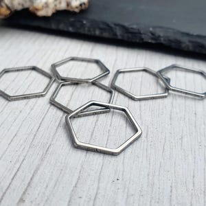 May include: Six silver hexagon rings, lying flat on a white surface. The rings are all the same size and shape, and they are arranged in a loose, overlapping pattern.