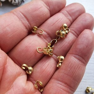 Pu&ograve; includere: Primo piano di una mano che tiene un gruppo di chiusure metalliche dorate. Le chiusure sono piccole e hanno una forma rotonda con un anello su un lato. Sono utilizzate per la creazione di gioielli o altri progetti di artigianato.