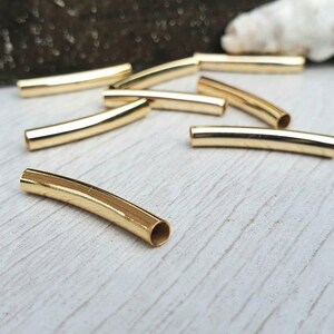 May include: A group of eight gold-coloured metal tube beads. The beads are curved and have a smooth, shiny finish.