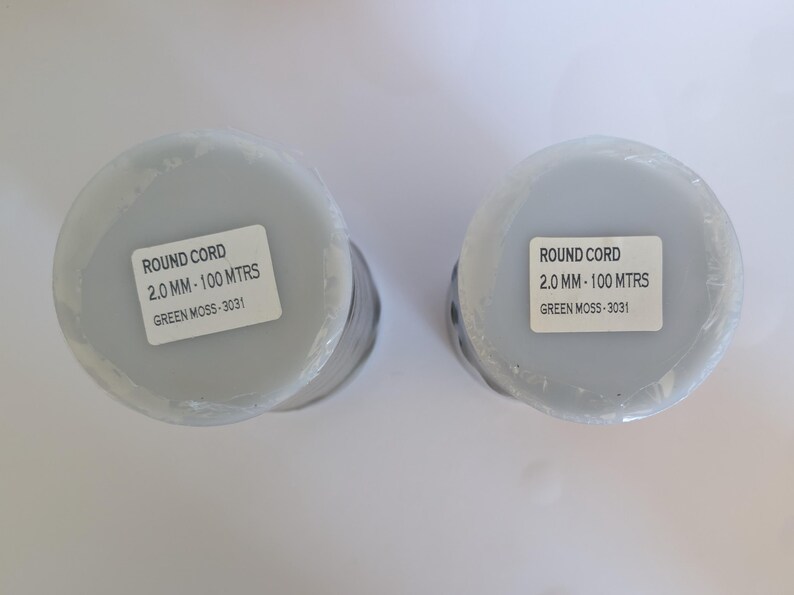 K&ouml;nnte beinhalten: Zwei Spulen mit Rundschnur, jede mit einem Etikett mit der Aufschrift "ROUND CORD 2.0 MM - 100 MTRS GREEN MOSS - 3031".