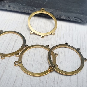 May include: A collection of brass-coloured metal circle charms, ideal for jewellery making. Each charm features small loops and holes. The charms are arranged on a light-coloured surface.