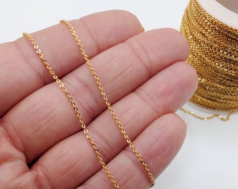 May include: Close-up of a gold-colored chain held in a hand, with a spool of chain visible in the background. The chain is made of small, interconnected links. The chain is a bright, shiny gold color.