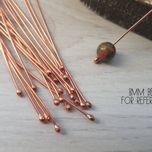 May include: A close-up of a pile of 20 copper head pins with rounded heads. The pins are approximately 1.5 inches long. An 8mm bead is shown for reference. 8MM BEAD FOR REFERENCE.