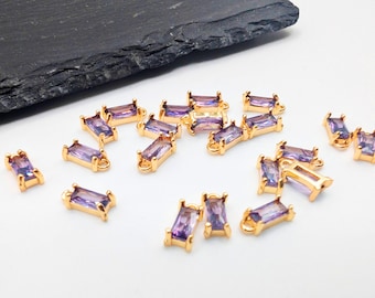 May include: A group of 18 gold-toned rectangular charms with purple iridescent glass stones. The charms have a loop at the top for attaching to jewelry.