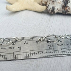 Może przedstawiać: Dwa srebrne metalowe zapięcia, każde o długości około 2,5 cm, pokazane są na linijce z oznaczeniami w calach i centymetrach. Linijka zawiera napis "Stainless Steel" i "1 Meter = 39.37 in".