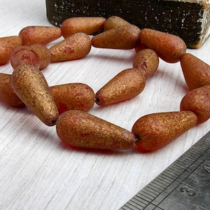 May include: A strand of red and gold pear-shaped glass beads. The beads have a textured, metallic finish.