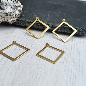 以下が含まれることがあります： 上部にループが付いた、金色の金属製のダイヤモンド型のペンダントチャームが4つ。チャームは白い木製の表面の上に置かれています。