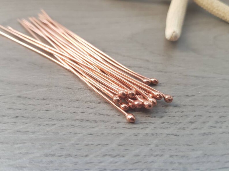 May include: A bundle of rose gold head pins with rounded ends. The pins are arranged in a fan shape on a wooden surface.