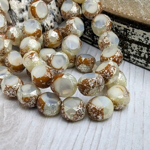 May include: A strand of iridescent white glass beads with a brown metallic finish. The beads are faceted and have a unique, textured look.