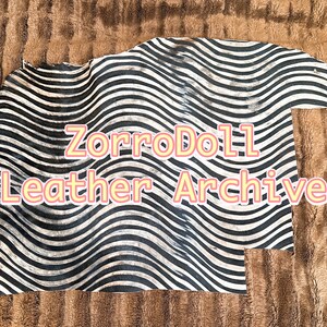 May include: A piece of leather with a black and white wavy striped pattern. The text "ZorroDoll Leather Archive" is displayed in a pink font across the leather. The background is a brown, textured fabric.