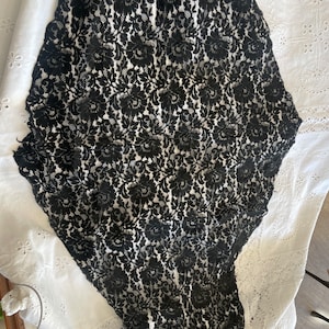 Puede incluir: Tela de encaje negra con un patrón floral. El encaje es delicado e intrincado, con un borde festoneado.