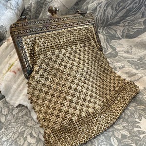 May include: An antique, open, beaded purse with a decorative metal frame. The purse features a detailed, geometric pattern in shades of gold and cream. The metal frame has an ornate design and a clasp closure.