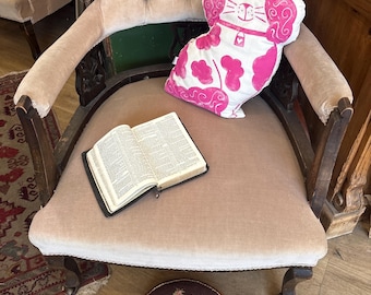 Un encantador taburete antiguo victoriano con una tapa de tapicería con bordado floral en ricos tonos rosados sobre un fondo marrón oscuro.