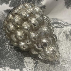 May include: A silver glass ornament shaped like a bunch of grapes. The ornament is made of many small, round, glass bubbles.