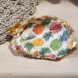 以下が含まれることがあります： パイナップルのプリントが施された、金色の縁取りのある白いセラミック製の皿。ジュエリーや鍵などの小さなものを置くのに最適です。