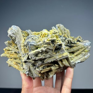 Może przedstawiać: Gromada szarych i żółtych kryształów mineralnych. Kryształy są długie i cienkie i ułożone w przypadkowy wzór. Minerał jest naturalnym okazem.