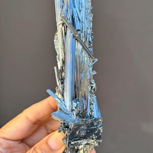 Könnte beinhalten: Ein großer, silberfarbener Kristallcluster mit schwarzer Basis. Der Kristall steht auf einem klaren Displayständer.