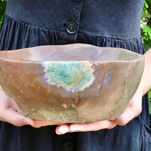 May include: A large, brown agate bowl with green and purple accents. The bowl is carved from a single piece of stone and has a natural, organic shape.