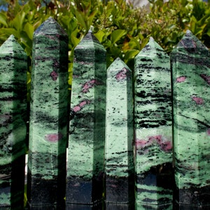 May include: Seven green, black and pink unakite crystal points arranged in a row on a silver tray. The points are all approximately the same size and shape, and they have a smooth, polished finish.