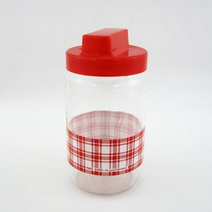 May include: A clear glass jar with a red lid and a red and white checked band around the middle. The jar has the text "felix potin - la parisienne" printed on the band.