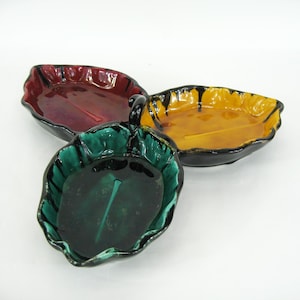 Può includere: Tre piatti in ceramica a forma di foglia nei toni del verde, bordeaux e giallo. Ogni piatto ha una finitura lucida e un bordo nero. I piatti sono disposti a triangolo.