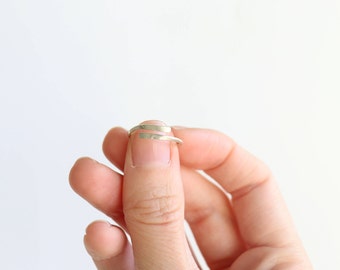 May include: A silver-colored ring with a spiral design. The ring wraps around the finger, creating a minimalist and modern look. The ring is held against a white background.
