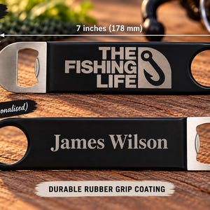 May include: A black bottle opener with a silver metal end, measuring 178 mm long and 38 mm wide. The front features the text THE FISHING LIFE with a hook icon, while the back is personalised with the name James Wilson in silver text.