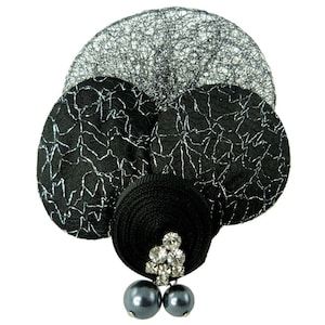 Può includere: Broche a forma di fiore in tessuto nero e argento con un centro di strass e due accenti di perle nere.