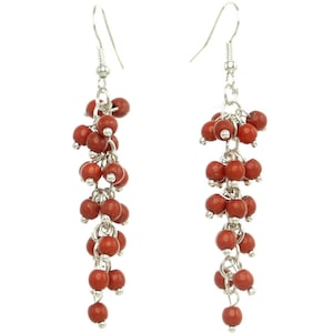 Può includere: Un paio di orecchini pendenti con un gruppo di piccole perle rosse appese a catene d'argento.
