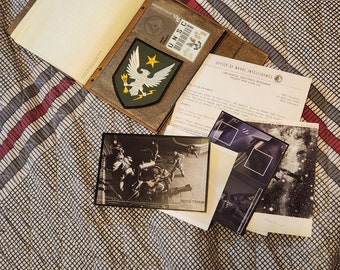 May include: A brown leather folder with a white eagle patch and the text "UNSC" on a white tag. The folder is open to reveal a document with the text "OFFICE OF NAVAL INTELLIGENCE" and a black and white photo of a group of soldiers.