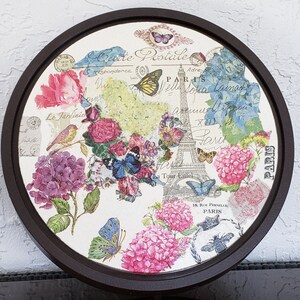 May include: A round wooden tray with a white background featuring a vintage Parisian design. The tray has a brown wooden frame and features a floral design with butterflies, birds, and the Eiffel Tower. The text "Carte Postale" is written in a cursive font at the top of the tray.