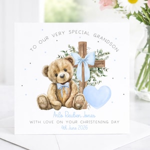 May include: A greeting card with a teddy bear, cross, and heart illustration. The card reads "TO OUR VERY SPECIAL GRANDSON" and includes the name "Arlo Reuben Jones" and the date "4th June 2026". The bear and heart are light blue.