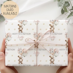 May include: Gift wrap featuring a repeating pattern of teddy bears holding balloons with the number 18, floral accents, and the name "Jodie." The words "Happy 18th Birthday" are also printed on the wrap. A matching card is available.