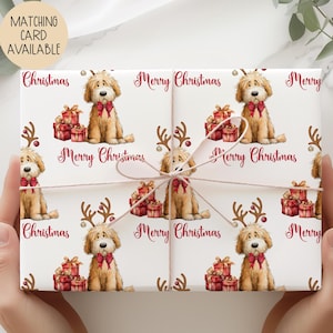 May include: White Christmas wrapping paper featuring a repeating pattern of a golden doodle dog wearing a red bow tie and reindeer antlers, with the words "Merry Christmas" in burgundy script. Presents are also included in the design.