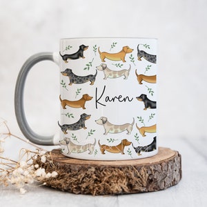 Puede incluir: Taza de cer&aacute;mica blanca con asa gris con un patr&oacute;n de perros salchicha de varios colores y poses. La taza tiene el nombre "Karen" escrito en ella.