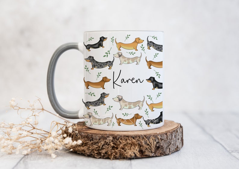 Puede incluir: Taza de cer&aacute;mica blanca con asa gris con un patr&oacute;n de perros salchicha de varios colores y poses. La taza tiene el nombre "Karen" escrito en ella.