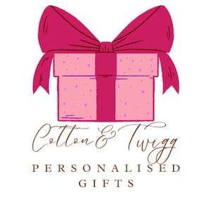 May include: A pink gift box with a magenta bow and ribbon. The box is decorated with small purple crosses. The text "Cotton & Twigg" is written in a cursive font above the words "Personalised Gifts".
