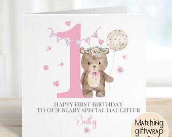 May include: A white birthday card featuring a pink number 1 and a brown teddy bear with a floral crown. The card says "Happy First Birthday To Our Beary Special Daughter Emily". The card is decorated with hearts and a balloon.