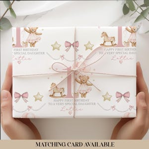 Personalised pink first birthday wrapping paper featuring a cute teddy bear in a tutu holding balloons, rocking horse, gold stars, pink bows, and the number one. Text reads “Happy First Birthday to a Very Special Daughter/Granddaughter/Any relation ” Ideal for baby girl’s first birthday gifts.