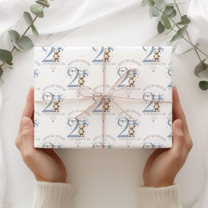 May include: A wrapped gift with a light pink ribbon. The wrapping paper is white with a repeating pattern of a teddy bear holding a star balloon, the number 2, and the text "HAPPY 2ND BIRTHDAY TO OUR WONDERFUL SON".