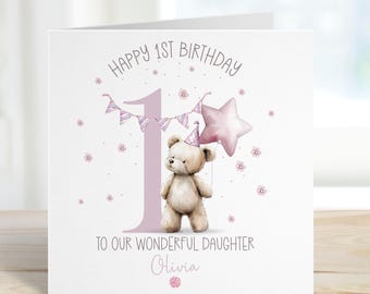 May include: A white greeting card with a light purple number 1 and text that reads "Happy 1st Birthday". The card features a teddy bear wearing a party hat and holding a pink star balloon. The text "To Our Wonderful Daughter Olivia" is also included.