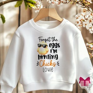 Puede incluir: Sudadera blanca con un pollito amarillo con gafas de sol y el texto "Forget the eggs I'm hunting chicks Louie".