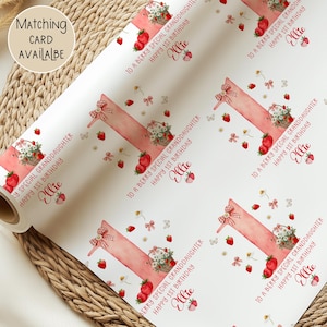 May include: White wrapping paper roll with a repeating pattern of strawberries, floral baskets, and the text "To a Berry Special Granddaughter Happy 1st Birthday Ellie". A matching card is available.