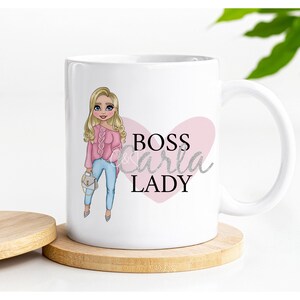 May include: White ceramic mug with a pink heart and the text "BOSS Carla LADY" in black and silver glitter. A cartoon illustration of a woman with blonde hair wearing a pink sweater and blue jeans is on the left side of the mug.