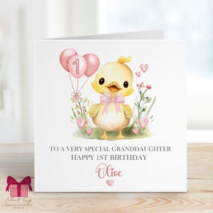 May include: A pink and white birthday card with a cute cartoon duckling holding pink balloons. The card says "To a very special granddaughter Happy 1st Birthday Olive".