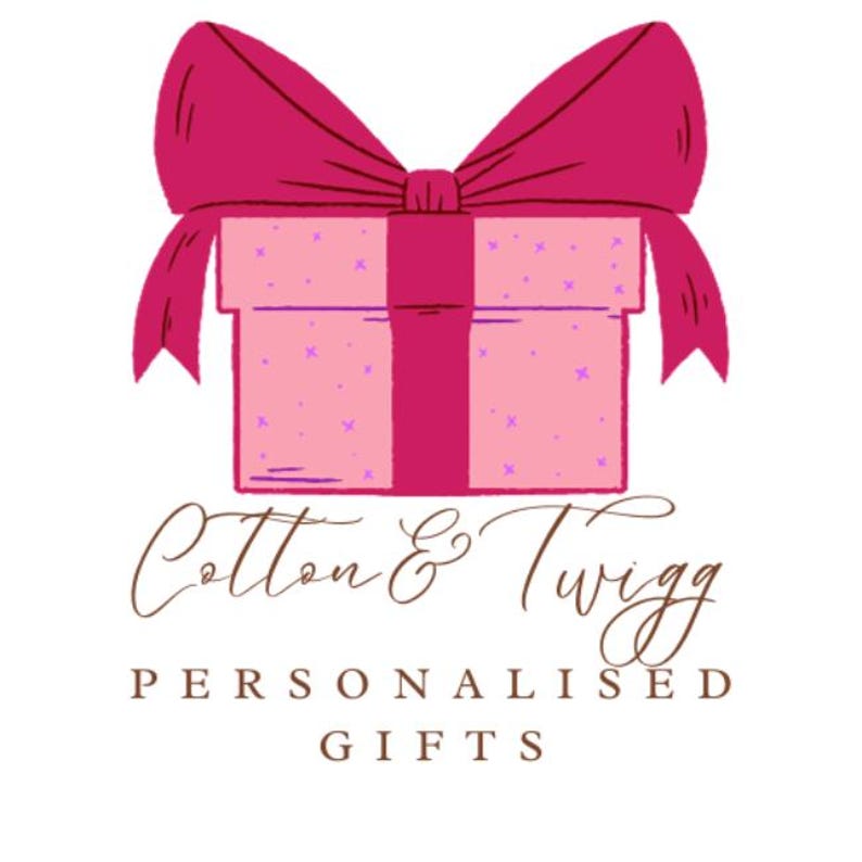May include: A pink gift box with a magenta bow and ribbon. The box is decorated with small purple crosses. The text "Cotton & Twigg" is written in a cursive font above the words "Personalised Gifts".