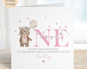 May include: A white first birthday card with a watercolour illustration. It features a teddy bear with a floral crown, a balloon, and the word "ONE" in pink. The text reads "Happy First Birthday to our Beary Special Granddaughter Dolly."